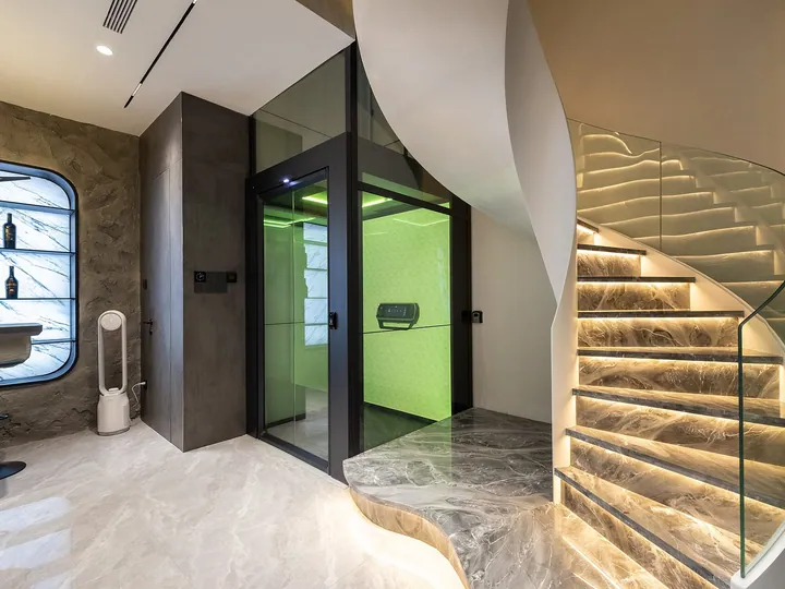 Round glass home elevator beside a staircase in a modern living room
